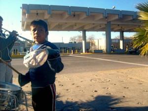 A boy from Juarez stands in the US - Mexican border begging for money.