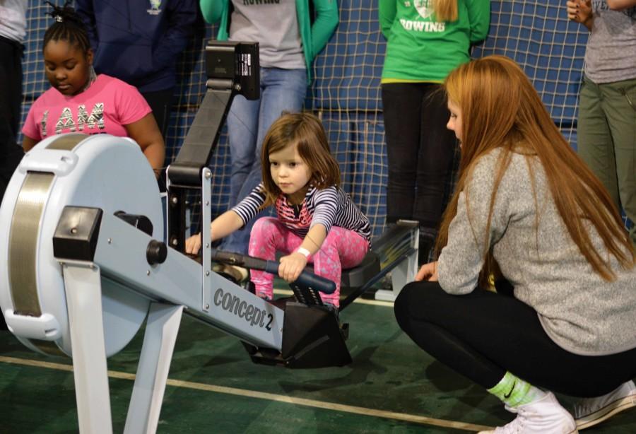Freshman+rower+Amelia+Kanonczyk+guides+a+young+girl+using+a+rowing+machine.+The+event+offered+activities+in+more+than+10+sports.